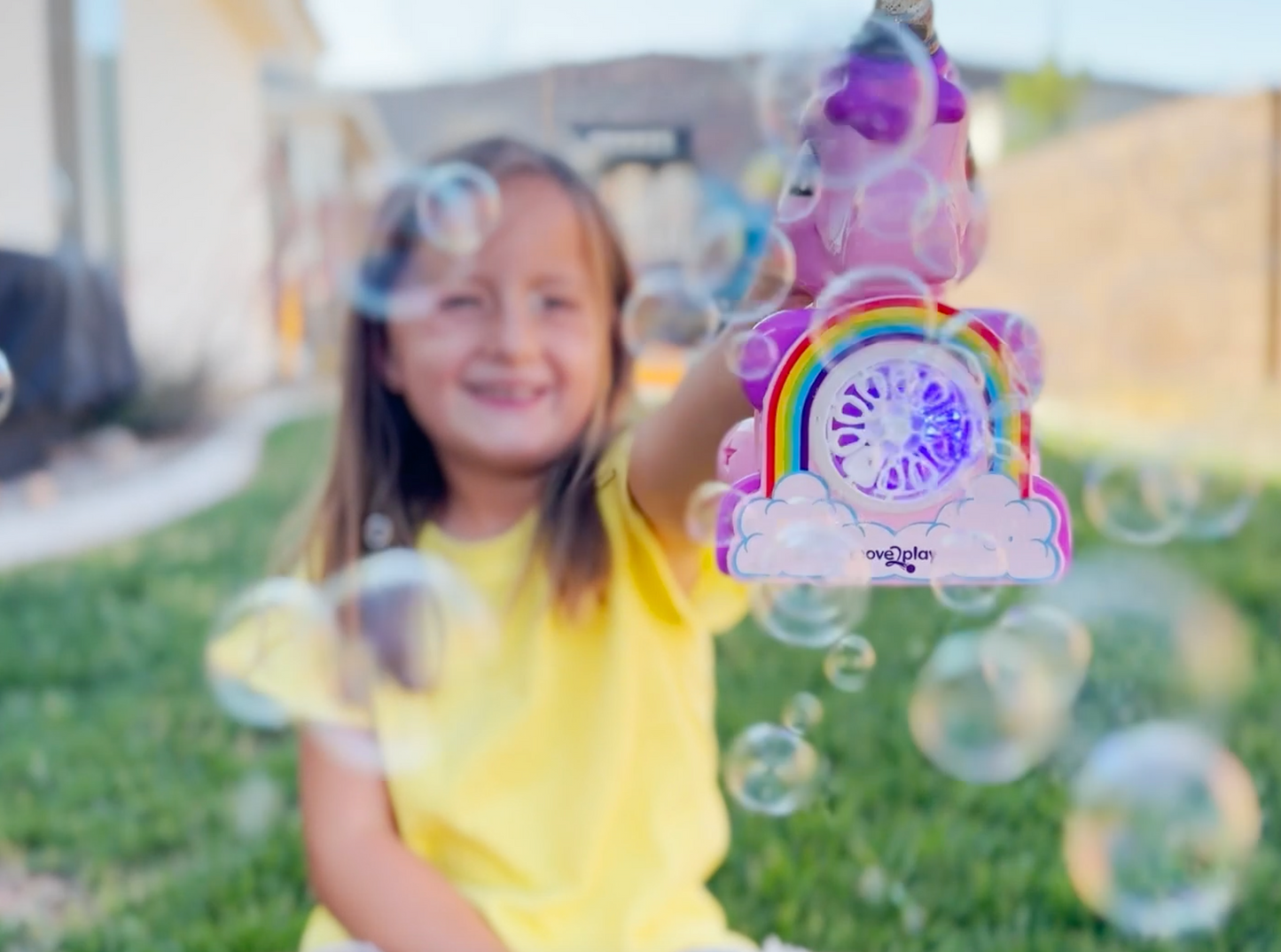 Child holding unicorn bubble blower toy with batteries and bubble solution included. Handheld design with durable, water-resistant features and easy-grip handle. Produces thousands of bubbles per minute for fun-filled occasions like birthdays and playdates.