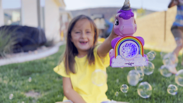 Child holding unicorn bubble blower toy with batteries and bubble solution included. Handheld design with durable, water-resistant features and easy-grip handle. Produces thousands of bubbles per minute for fun-filled occasions like birthdays and playdates.